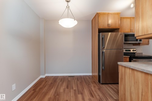 Kitchen area featuring wood-finish flooring, light wood cabinetry, and stainless steel appliances including a refrigerator, microwave, and range - 16B Callingwood Court, Edmonton, AB 