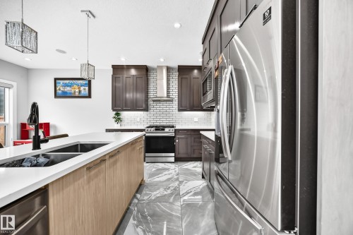 Modern kitchen featuring a large island with an undermount double sink and black faucet - 8710 Mayday Lane, Edmonton, AB 