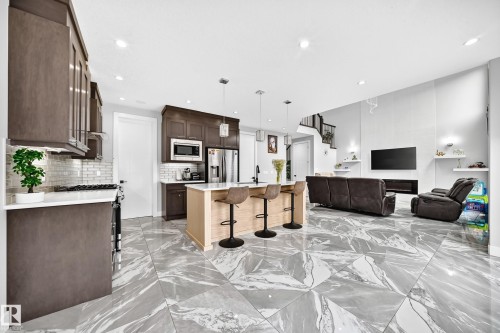 Open-concept living space featuring large format marble-look tile flooring, a kitchen island with seating, dark wood-finish cabinetry, a subway tile backsplash, and recessed lighting - 8710 Mayday Lane, Edmonton, AB 