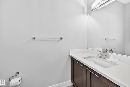 Bathroom vanity featuring a rectangular integrated sink, white countertop, and dark wood-finish cabinetry with silver hardware - 8710 Mayday Lane, Edmonton, AB 