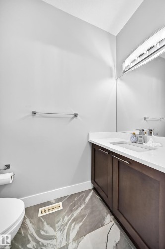 Vanity featuring a white countertop, dark wood-finish cabinetry with silver hardware, and an integrated sink - 8710 Mayday Lane, Edmonton, AB 