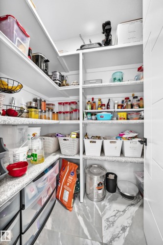 Walk-in pantry featuring extensive built-in shelving, durable countertop space, integrated drawer storage, and marble-look floor tiling - 8710 Mayday Lane, Edmonton, AB 