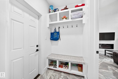 Entryway featuring a white paneled door with matte black hardware, built-in storage bench with a speckled countertop, integrated shelving, and wall-mounted hooks - 8710 Mayday Lane, Edmonton, AB 