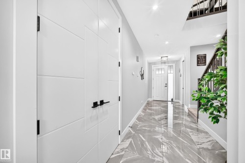 Hallway featuring grey marble-look tile flooring, white doors with modern black hardware, recessed lighting, and a staircase with dark wood-finish railings - 8710 Mayday Lane, Edmonton, AB 