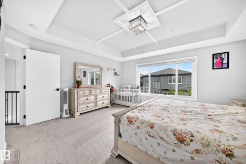 Carpeted bedroom featuring a coffered ceiling with a central chandelier, a large window, and a built-in railing - 8710 Mayday Lane, Edmonton, AB 