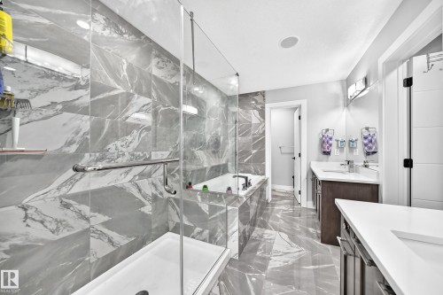 Spacious bathroom featuring a glass-enclosed shower, a separate soaking tub, dual vanity with undermount sinks, and large format marble-look tile flooring and shower surround - 8710 Mayday Lane, Edmonton, AB 