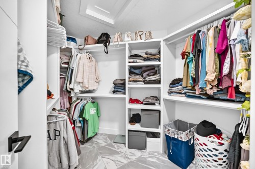 Walk-in closet featuring white shelving, multiple hanging rods, built-in shelving units, and marble-look flooring - 8710 Mayday Lane, Edmonton, AB 