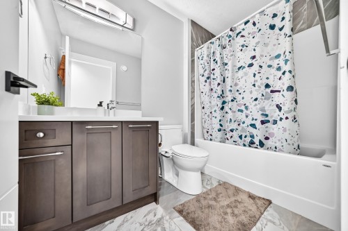 Bathroom featuring a dark wood-finish vanity with a white countertop, a built-in bathtub with a shower, a wall-mounted mirror, and marble-look floor tiling - 8710 Mayday Lane, Edmonton, AB 