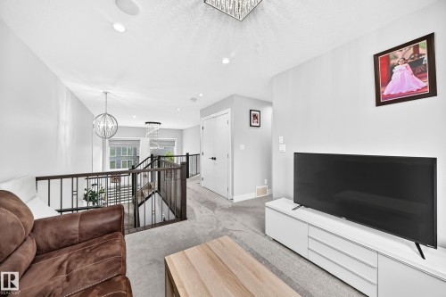 Open concept landing featuring a modern black metal and wood railing, recessed lighting, and a contemporary chandelier - 8710 Mayday Lane, Edmonton, AB 