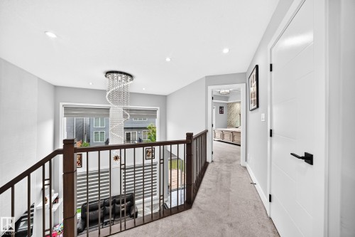 Contemporary upper-level hallway featuring a striking spiral chandelier, dark wood-finish railings, and recessed lighting - 8710 Mayday Lane, Edmonton, AB 