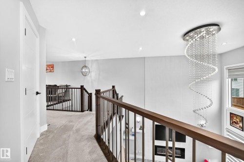 Upper-level hallway with plush gray carpeting and a contemporary spiral chandelier - 8710 Mayday Lane, Edmonton, AB 