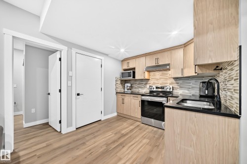 Kitchen featuring light wood-finish cabinetry, dark countertops, stainless steel appliances, and a textured tile backsplash - 8710 Mayday Lane, Edmonton, AB 