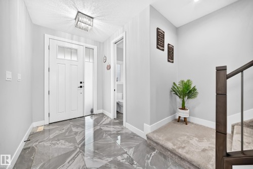 Foyer featuring a white front door with transom and sidelight, large format gray marble-look tile flooring, and a contemporary crystal flush mount light fixture - 8710 Mayday Lane, Edmonton, AB 