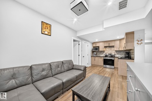 Open-concept living space featuring wood-finish flooring, recessed lighting, and a modern kitchen - 8710 Mayday Lane, Edmonton, AB 