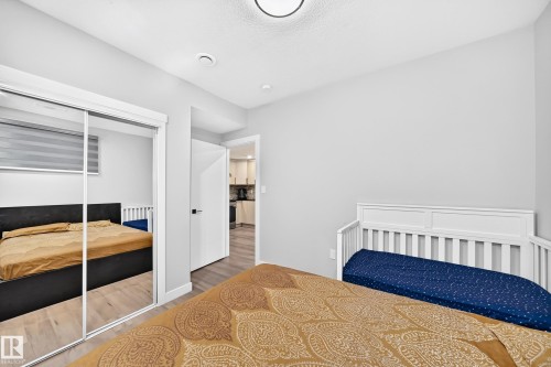 Bedroom featuring light wood-finish flooring, a full-height mirrored closet, a recessed ceiling light, and a white interior door with dark hardware - 8710 Mayday Lane, Edmonton, AB 