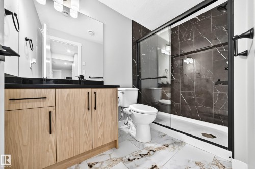 Modern bathroom featuring a wood-finish vanity with a dark countertop and black hardware - 8710 Mayday Lane, Edmonton, AB 