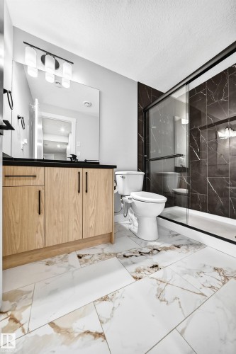 Modern bathroom featuring a wood-finish vanity with a black countertop, a full-width mirror, and a contemporary light fixture - 8710 Mayday Lane, Edmonton, AB 
