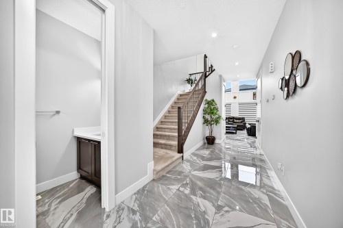 Hallway featuring large format marble-look tile flooring and a carpeted staircase with dark wood railings - 8710 Mayday Lane, Edmonton, AB 