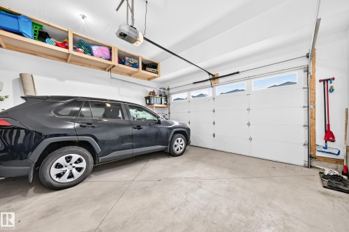 Two-car garage featuring a white overhead door with upper windows, concrete flooring, and built-in overhead wooden shelving - 8710 Mayday Lane, Edmonton, AB 
