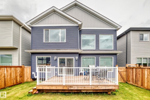 Rear exterior featuring a spacious wood-finish deck with white railing, blue horizontal siding, and multiple windows - 8710 Mayday Lane, Edmonton, AB 