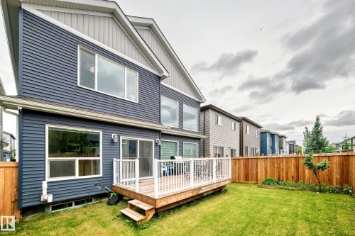 Rear exterior featuring blue horizontal siding, a wooden deck with white railings, a green lawn, and a light wood privacy fence - 8710 Mayday Lane, Edmonton, AB 