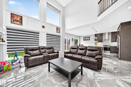 Two-story living area with high ceilings and large windows, featuring contemporary marble-look tile flooring - 8710 Mayday Lane, Edmonton, AB 