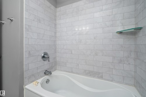 Bathtub with white subway tile surround, chrome fixtures, and a corner glass shelf - 5516 47A Avenue, Wetaskiwin, AB - Indoor Photo Showing Bathroom