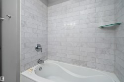 Bathtub with white subway tile surround, chrome fixtures, and a corner glass shelf - 