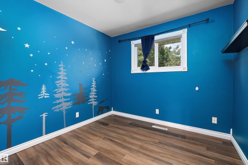 Room featuring wood-finish flooring, a bright blue wall with a forest mural, white baseboards, and a window with white trim - 5516 47A Avenue, Wetaskiwin, AB - Indoor Photo Showing Other Room