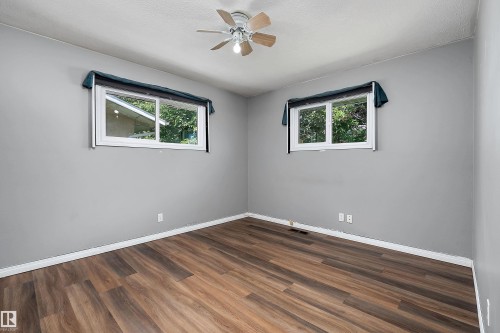 Room featuring wood-finish flooring, two windows, a ceiling fan with integrated lighting, and gray wall finishes - 5516 47A Avenue, Wetaskiwin, AB - Indoor Photo Showing Other Room