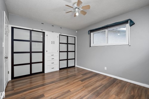 Wood-finish flooring throughout, featuring a ceiling fan with light fixture, built-in storage cabinetry with drawers, and sliding closet doors with frosted panels - 5516 47A Avenue, Wetaskiwin, AB - Indoor Photo Showing Other Room