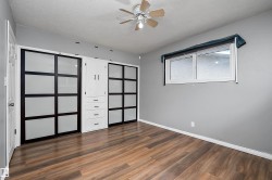 Wood-finish flooring throughout, featuring a ceiling fan with light fixture, built-in storage cabinetry with drawers, and sliding closet doors with frosted panels - 