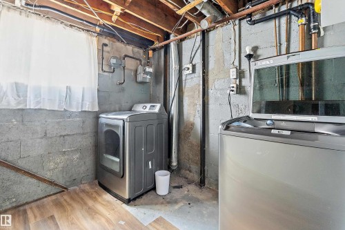 Utility space featuring exposed ceiling joists, concrete block walls, and a window with white sheers - 5516 47A Avenue, Wetaskiwin, AB - Indoor Photo Showing Laundry Room