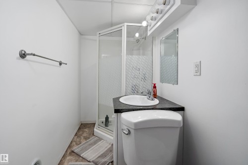 Full bathroom featuring a corner shower with frosted glass, a vanity with a white basin and dark countertop, a toilet, and a wall-mounted mirror with overhead lighting - 5516 47A Avenue, Wetaskiwin, AB - Indoor Photo Showing Bathroom