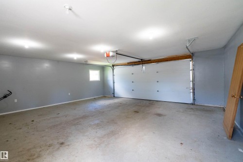 Spacious garage featuring a concrete floor, light gray walls, white ceiling, and a white overhead garage door with an automatic opener - 5516 47A Avenue, Wetaskiwin, AB - Indoor Photo Showing Garage