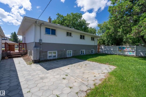 Rear exterior featuring white siding with a gray lower accent, multiple windows, a patterned paver patio, and a grassy area - 5516 47A Avenue, Wetaskiwin, AB - Outdoor