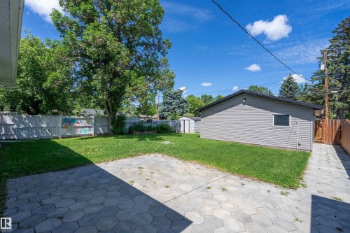Spacious backyard featuring a large paver patio, manicured lawn, perimeter fencing, mature trees, and a detached structure with horizontal siding - 5516 47A Avenue, Wetaskiwin, AB - Outdoor