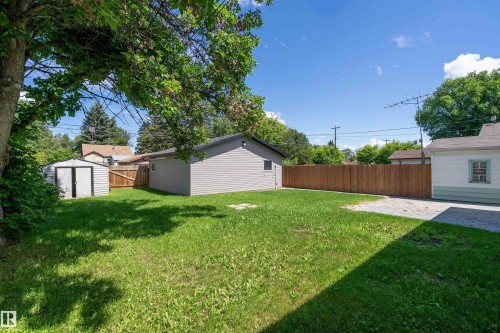 Expansive backyard featuring a manicured lawn, a detached garage with gray siding, a separate storage shed, a wood privacy fence, and paved areas - 5516 47A Avenue, Wetaskiwin, AB - Outdoor
