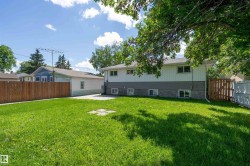 Expansive rear yard featuring a manicured lawn, established perimeter fencing, and mature trees providing natural shade - 