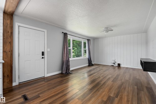 Spacious room featuring wood-finish flooring, a contemporary white entry door, a multi-pane window, and a white paneled accent wall - 5516 47A Avenue, Wetaskiwin, AB - Indoor Photo Showing Other Room