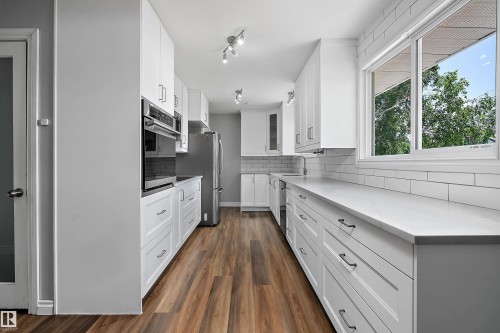 Contemporary kitchen featuring wood-finish flooring, white shaker cabinetry, stainless steel appliances, and a subway tile backsplash - 5516 47A Avenue, Wetaskiwin, AB - Indoor Photo Showing Kitchen With Upgraded Kitchen