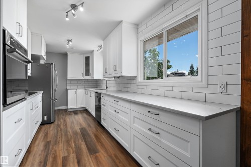 Kitchen featuring white shaker-style cabinetry, stainless steel appliances, light-toned countertops, subway tile backsplash, and wood-finish flooring - 5516 47A Avenue, Wetaskiwin, AB - Indoor Photo Showing Kitchen With Upgraded Kitchen