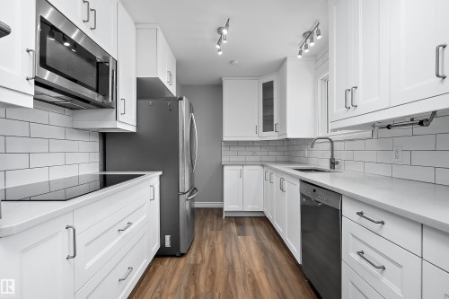Contemporary kitchen featuring white cabinetry, stainless steel appliances, light countertops, subway tile backsplash, and wood-finish flooring - 5516 47A Avenue, Wetaskiwin, AB - Indoor Photo Showing Kitchen With Stainless Steel Kitchen With Upgraded Kitchen