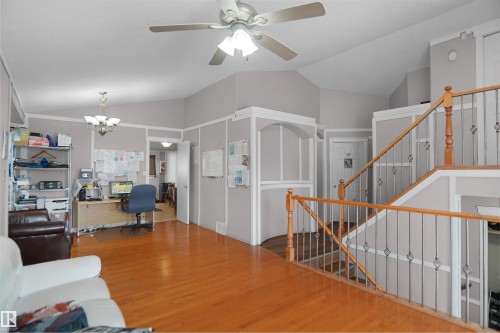 Open concept living area featuring wood-finish flooring, vaulted ceilings, a ceiling fan with integrated lighting, and a staircase with wood railing and iron balusters - 4816 155 Ave, Edmonton, AB 