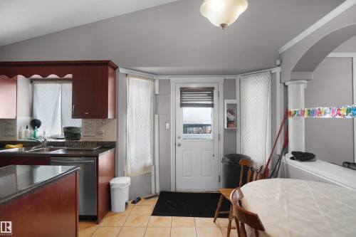 Kitchen featuring rich wood-finish cabinetry, dark countertops, a stainless steel dishwasher, and ceramic tile flooring - 4816 155 Ave, Edmonton, AB 