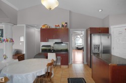 Kitchen area featuring vaulted ceilings, tile flooring, wood-finish cabinetry, a stainless steel refrigerator with a water/ice dispenser, and a granite-style countertop on the island - 
