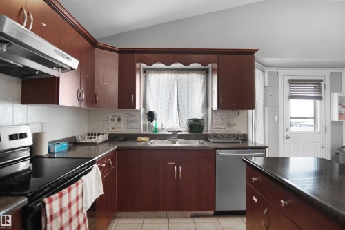 Kitchen featuring rich wood-finish cabinetry, dark countertops, and a white tile backsplash - 4816 155 Ave, Edmonton, AB 