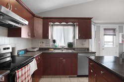 Kitchen featuring rich wood-finish cabinetry, dark countertops, and a white tile backsplash - 