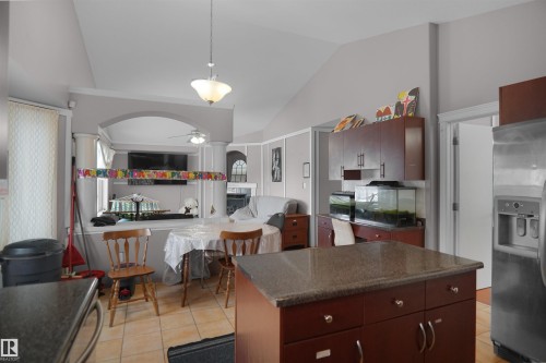 Kitchen featuring a central island with a granite-style countertop, mahogany-finish cabinetry, and ceramic tile flooring - 4816 155 Ave, Edmonton, AB 