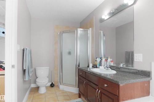Bathroom featuring a corner shower with glass enclosure, wood-finish vanity with a dark countertop, white toilet, and tile flooring - 4816 155 Ave, Edmonton, AB 